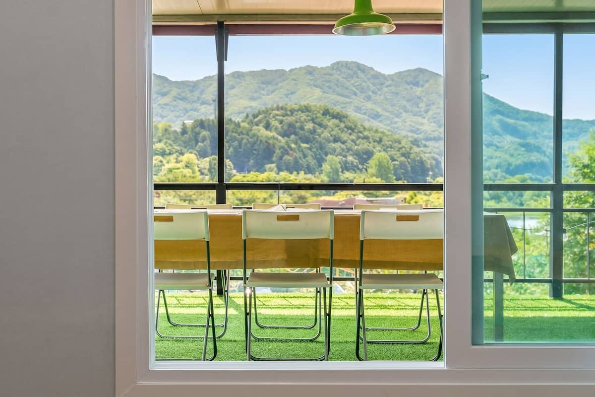 Une pièce dotée d’une grande fenêtre donnant sur un paysage montagneux, d’une table avec des chaises et d’un luminaire suspendu.