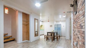 A spacious living area with a wooden floor, a dining table with benches, a kitchen in the background, and a brick accent wall. - Gapyeong Four Season Pension (Gapyeong)