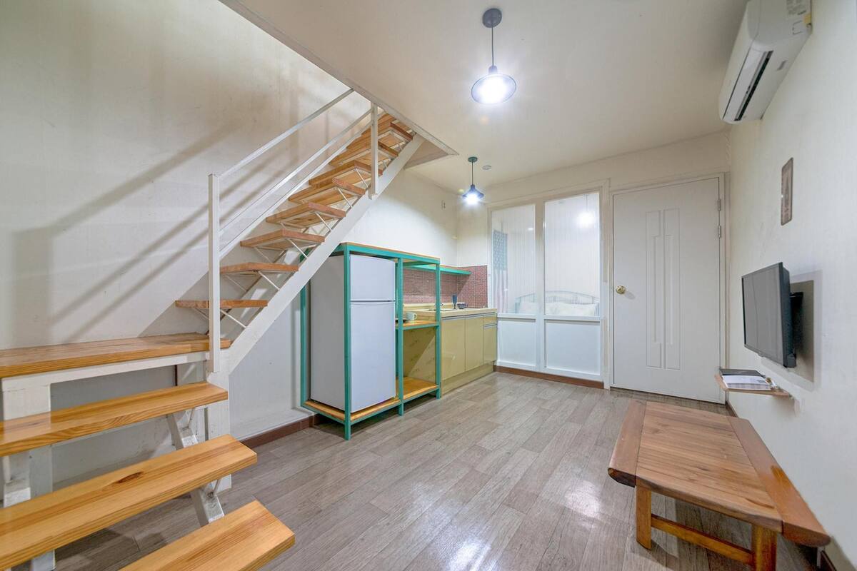 Un vaste espace de vie comprenant un escalier en bois, un coin cuisine et une table à manger.