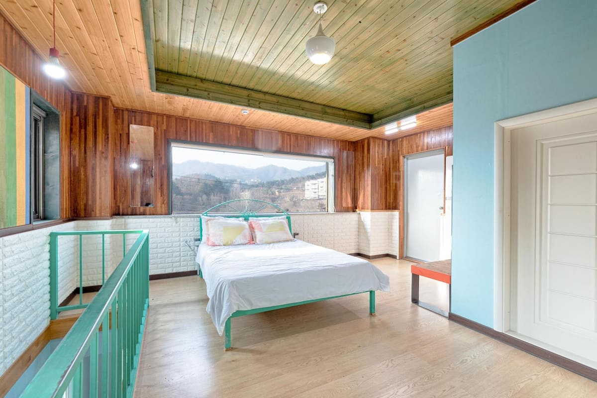 Une chambre à coucher avec un lit, une fenêtre donnant sur un beau paysage, un plafond en bois et une porte blanche.