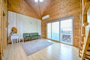Relax in this spacious room with a high ceiling, featuring a sliding glass door to an outdoor deck and a comfortable sofa.