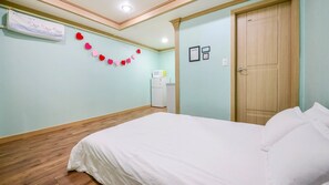A bedroom with a bed, a wooden floor, a wall-mounted heater, and a door. - Sokcho Dderak Pension (Sokcho)