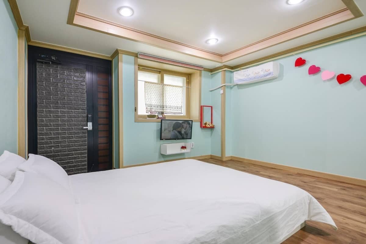 A bedroom with a bed, a window, a TV, and a wall with heart decorations.