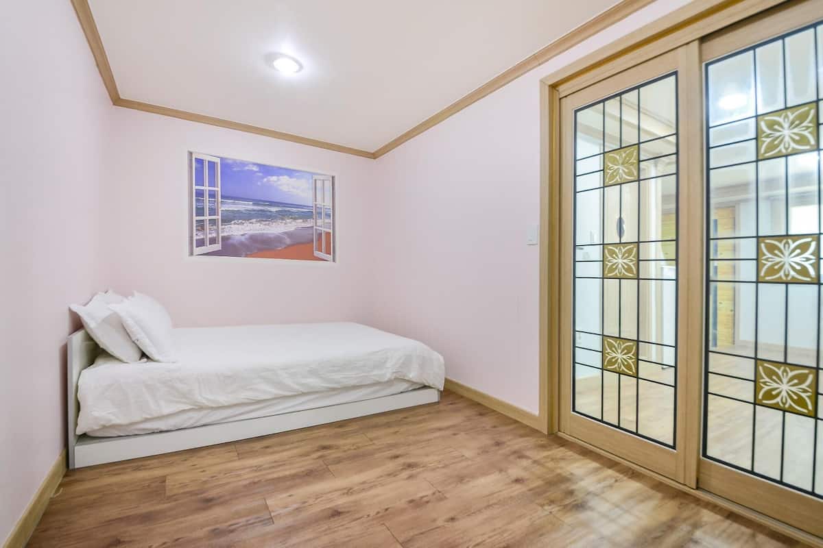 A bedroom with a bed, a window with a beach view, and a sliding glass door with decorative panels.