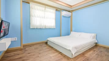 Een slaapkamer met een bed, een raam met gordijnen, een wandairconditioner en een televisie aan de linkerkant.