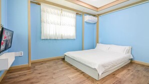 A bedroom with a bed, a window with curtains, a wall-mounted air conditioner, and a television on the left. - Sokcho Dderak Pension (Sokcho)