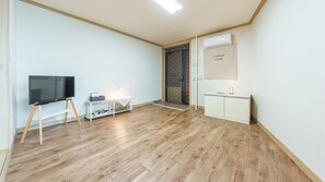 A room with a flat-screen TV on a stand, a small table with a lamp, a white cabinet, and a door with a brick pattern. - Sokcho Dderak Pension (Sokcho)