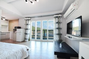 A modern bedroom with a large bed, a TV, and a balcony with a view of greenery. - Namhae Liebe Pension (Namhae)