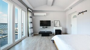 A modern bedroom with a large bed, a TV mounted on the wall, and a sliding glass door leading to an outdoor area. - Namhae Liebe Pension (Namhae)