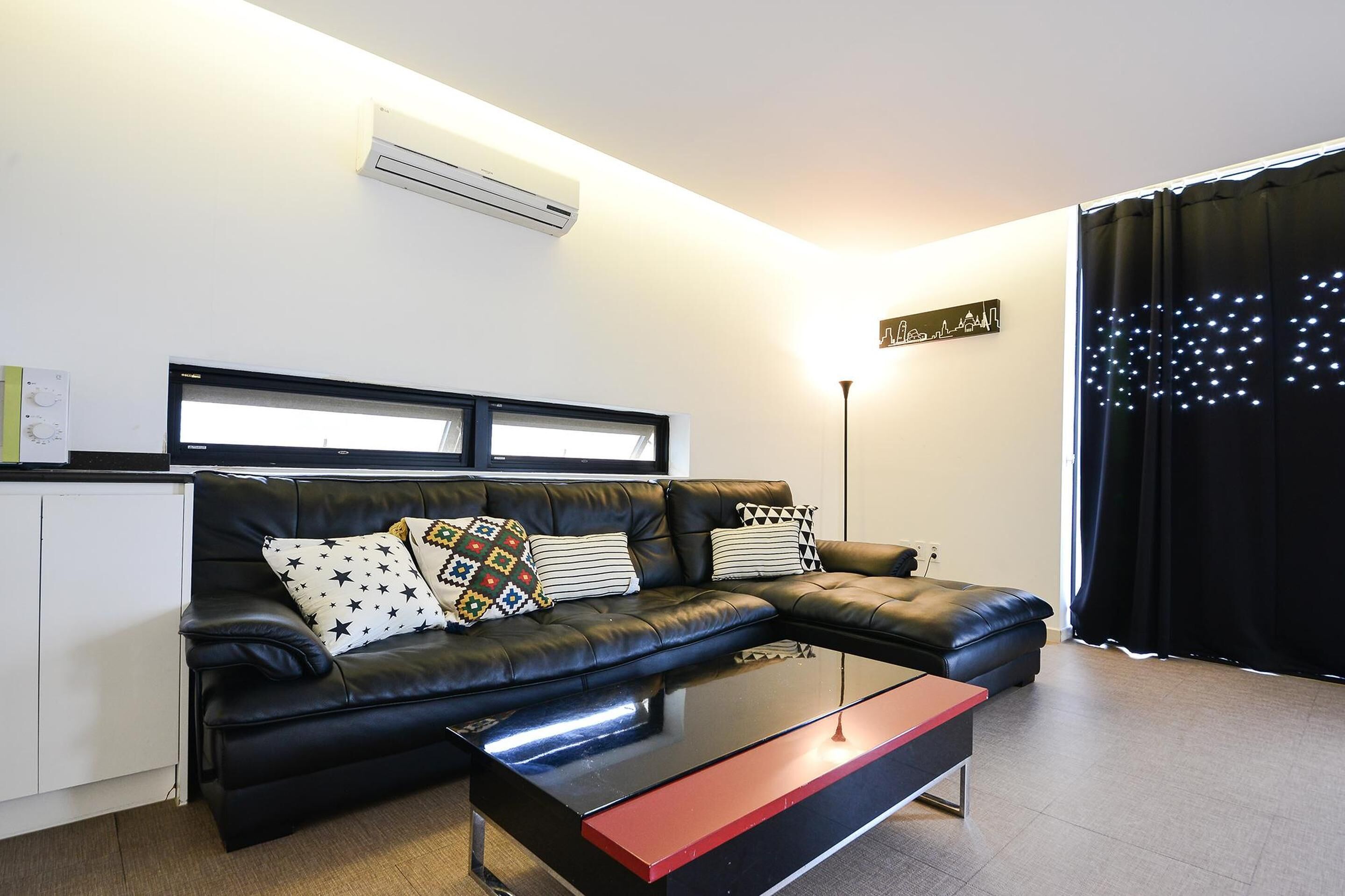 A modern living room with a black leather sofa, a glass coffee table, and a black curtain with LED lights.