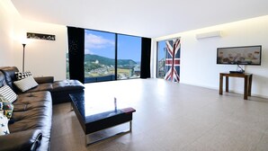 A modern living room with a leather sofa, a coffee table, and a large window offering a scenic view. - Namhae Liebe Pension (Namhae)