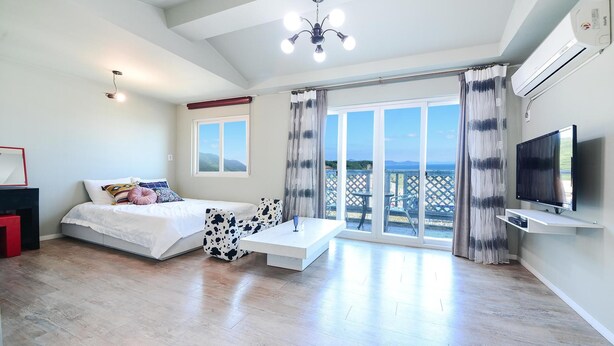 A modern bedroom with a bed, a sofa, a coffee table, a TV, and a balcony with a view. - Namhae Liebe Pension (Namhae)