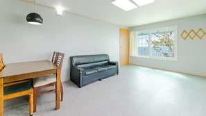 A room with a dining table and chairs, a leather sofa, a large window with a view, and a ceiling light fixture.