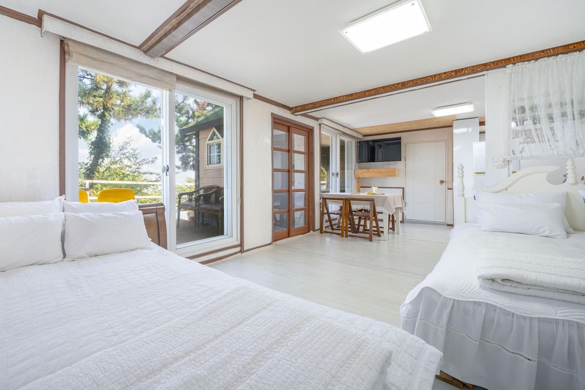 A hotel room with two beds, a dining table, and a sliding glass door leading to an outdoor area.
