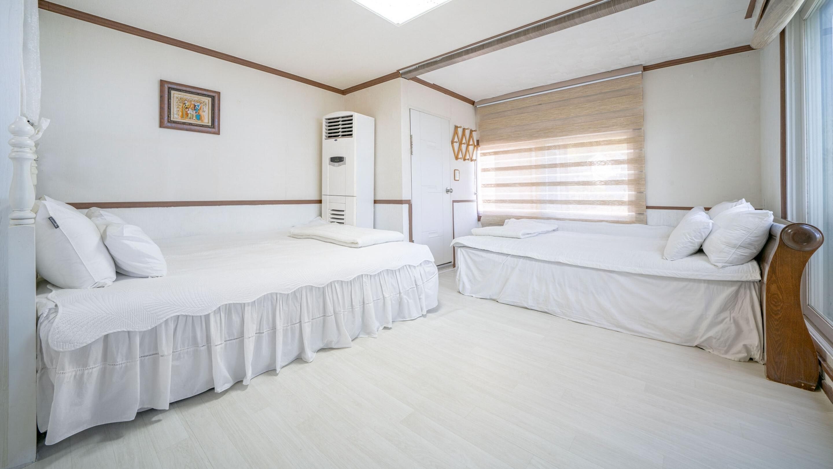 Ein Hotelzimmer mit zwei Betten, einem Schrank, einem Heizkörper und einem Fenster mit Jalousien.
