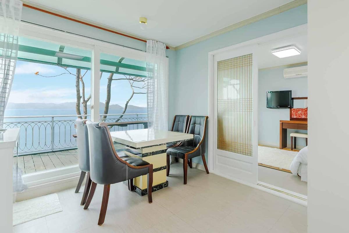 A room with a balcony, a dining table with chairs, a television, and a wardrobe.