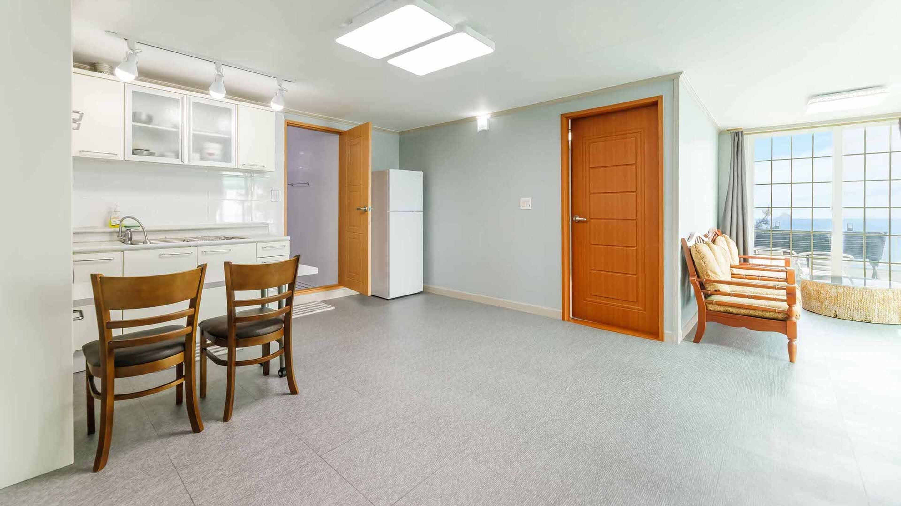 A modern kitchen with white cabinets, a dining area with two wooden chairs, and a large window with a view.