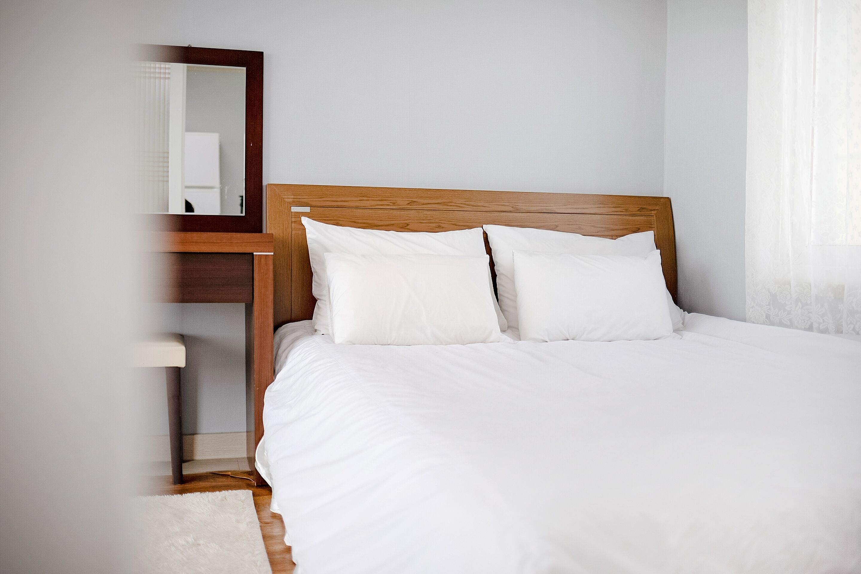 A neatly made bed with white linens and a wooden headboard, a small bedside table, and a mirror on the wall.