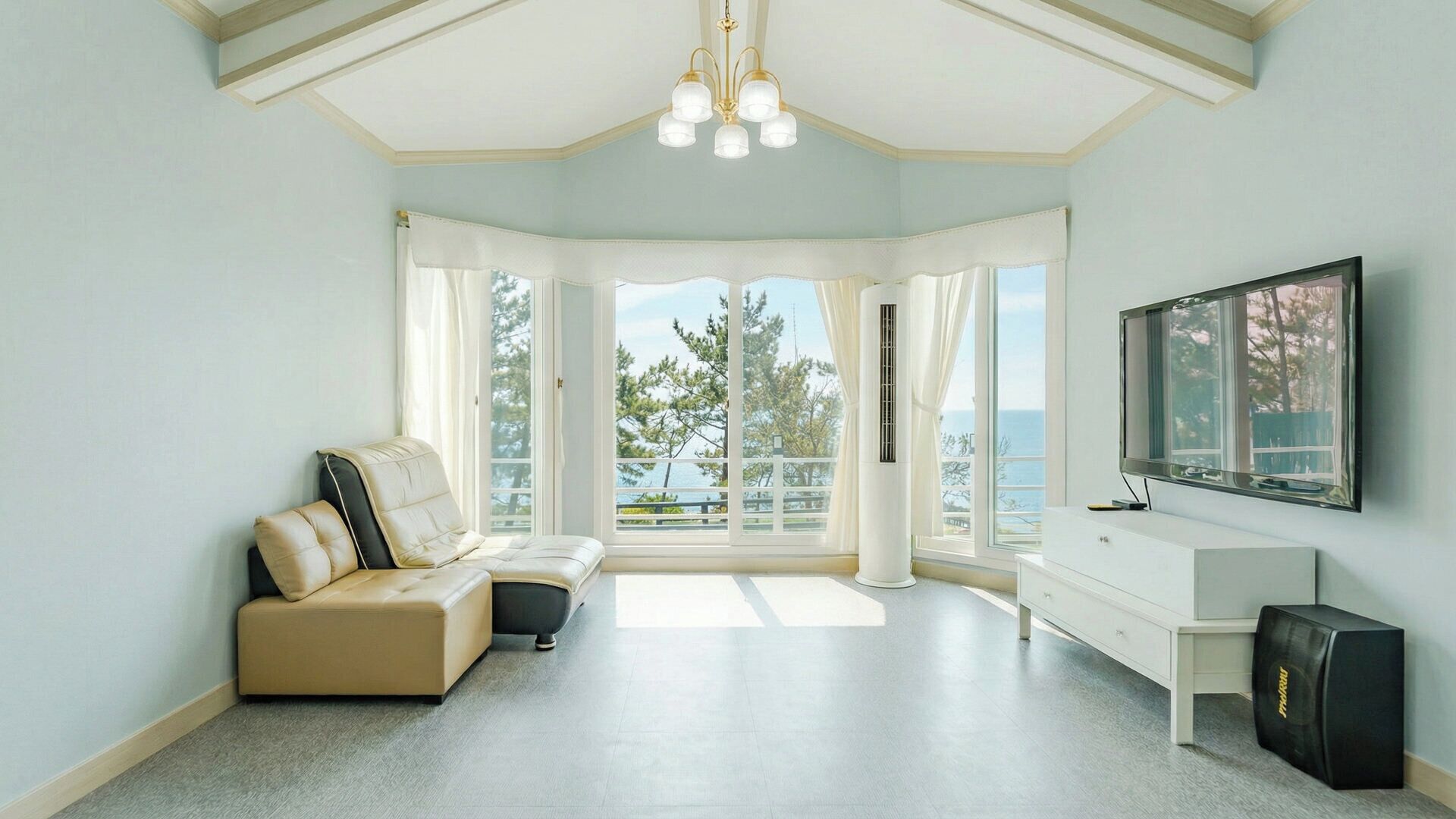 Una habitación con sofá, televisión, escritorio y un amplio ventanal con vista al mar.