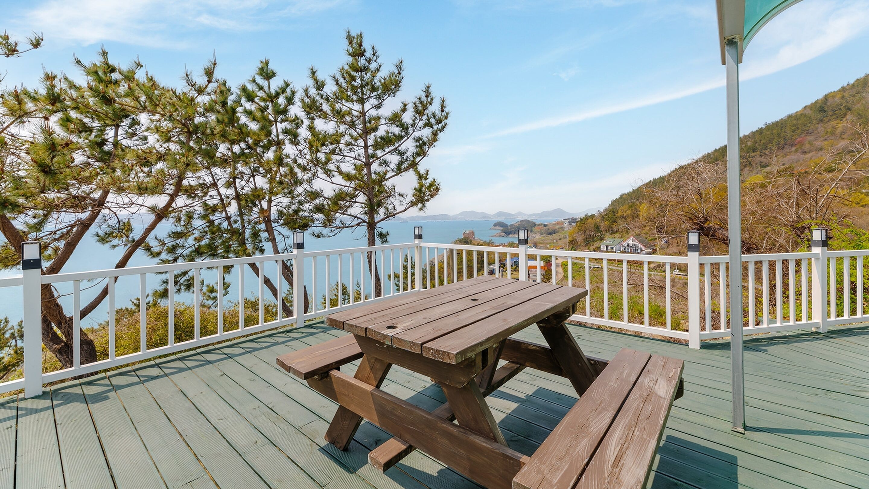 A wooden deck with a picnic table and white railing, overlooking a body of water and hills.