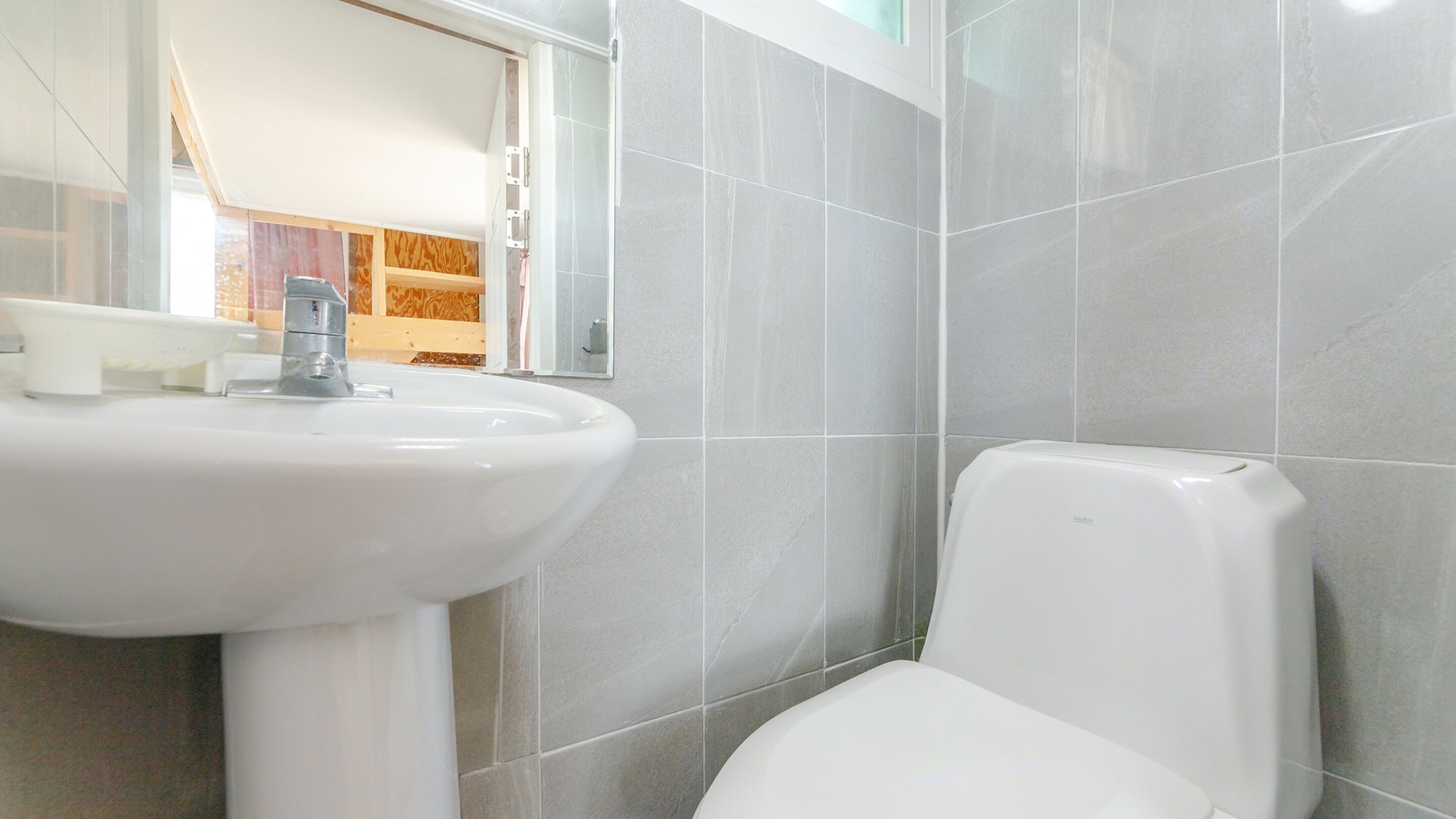 A bathroom with a white sink, a toilet, and grey tiled walls.