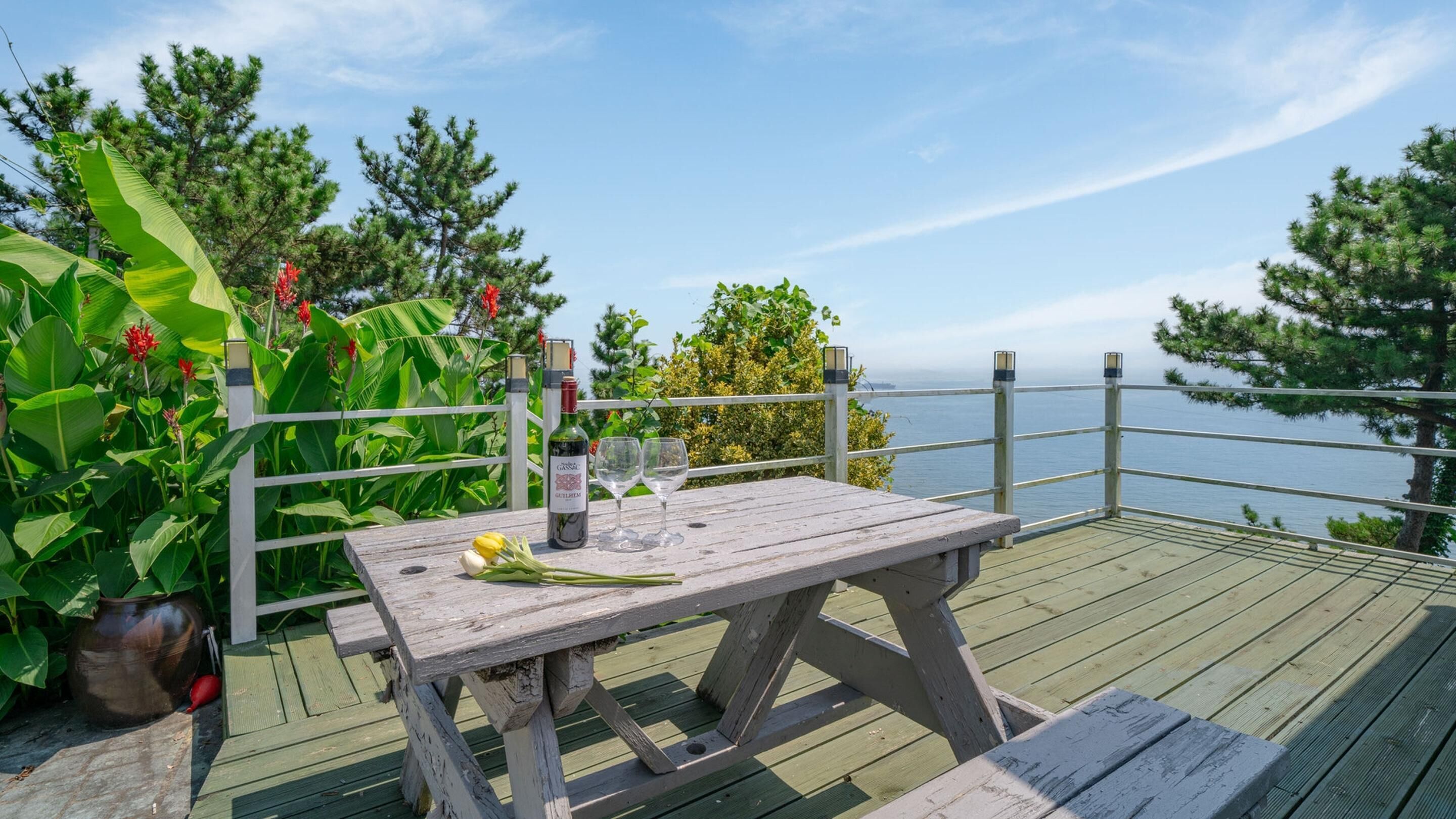 A wooden deck with a table set for two, overlooking a body of water.