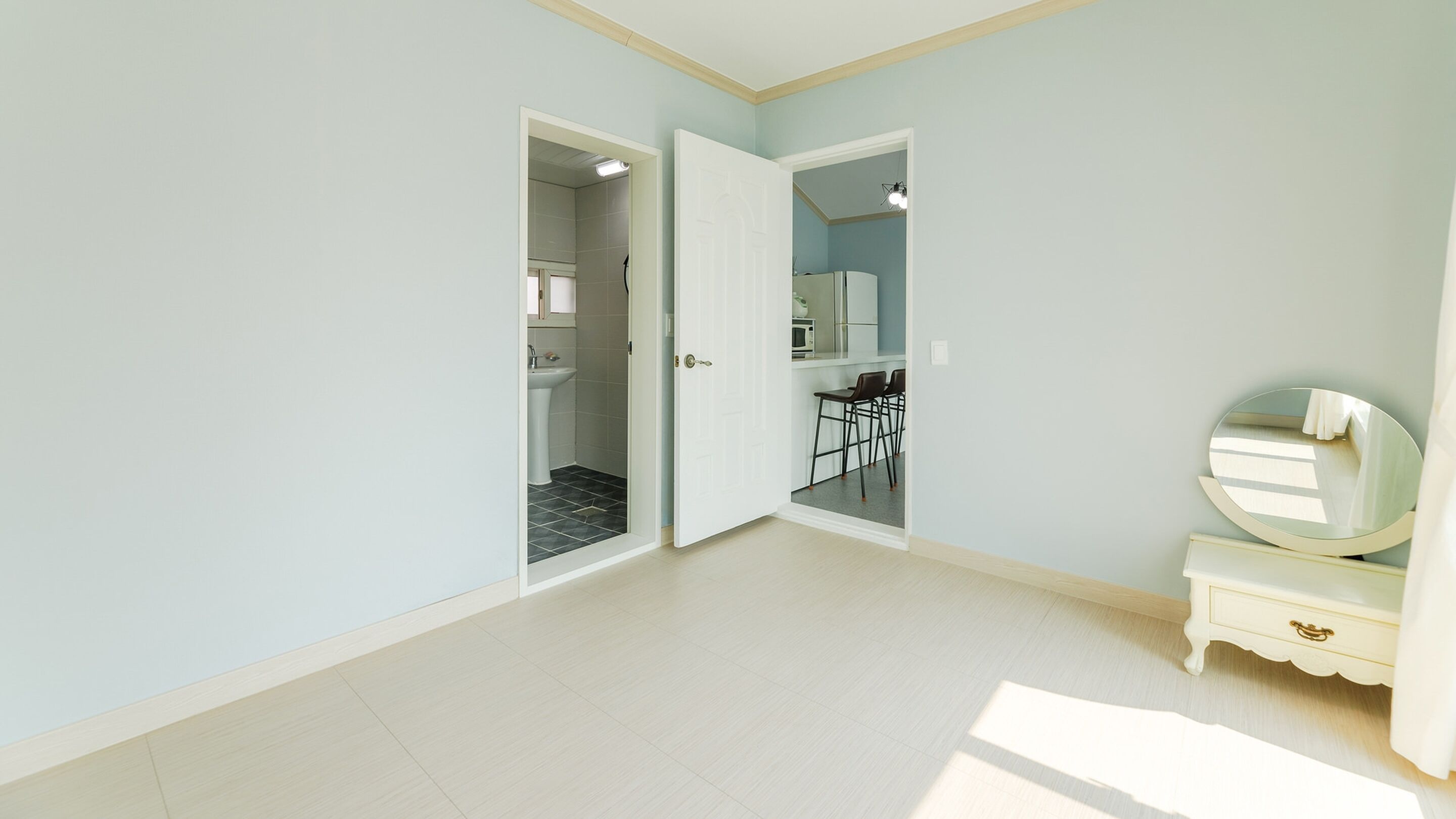Una habitación amplia con paredes azul claro, piso blanco y una puerta que da a un baño.