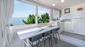 Een compacte keuken met uitzicht op zee, een eethoek met een tafel en stoelen, en een koelkast.