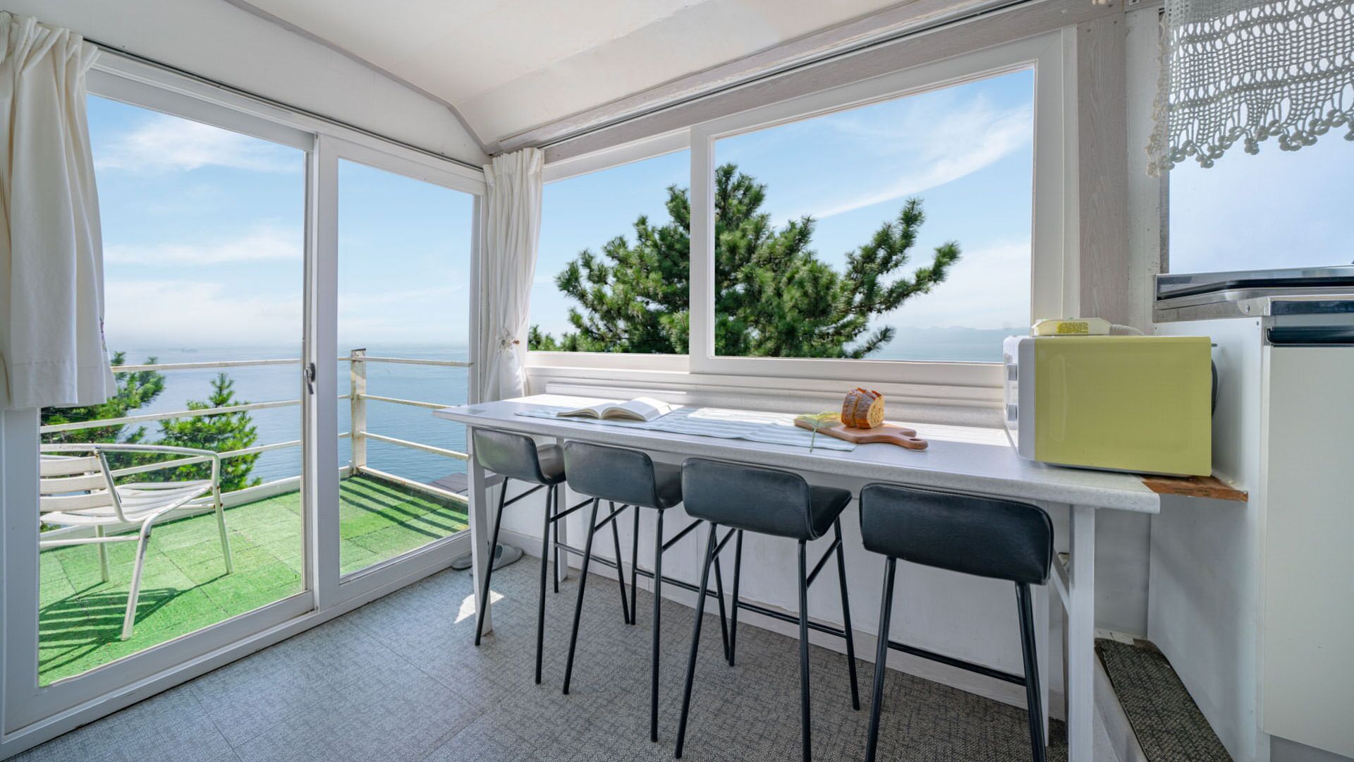 A balcony with a view of the sea and trees, a table with chairs, and a yellow appliance.