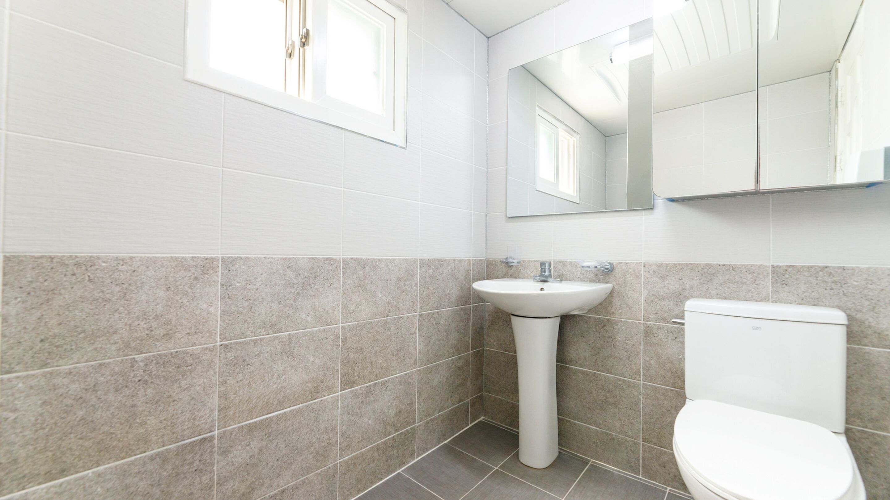 Une salle de bain avec des carreaux blancs, un lavabo, des toilettes et un miroir.