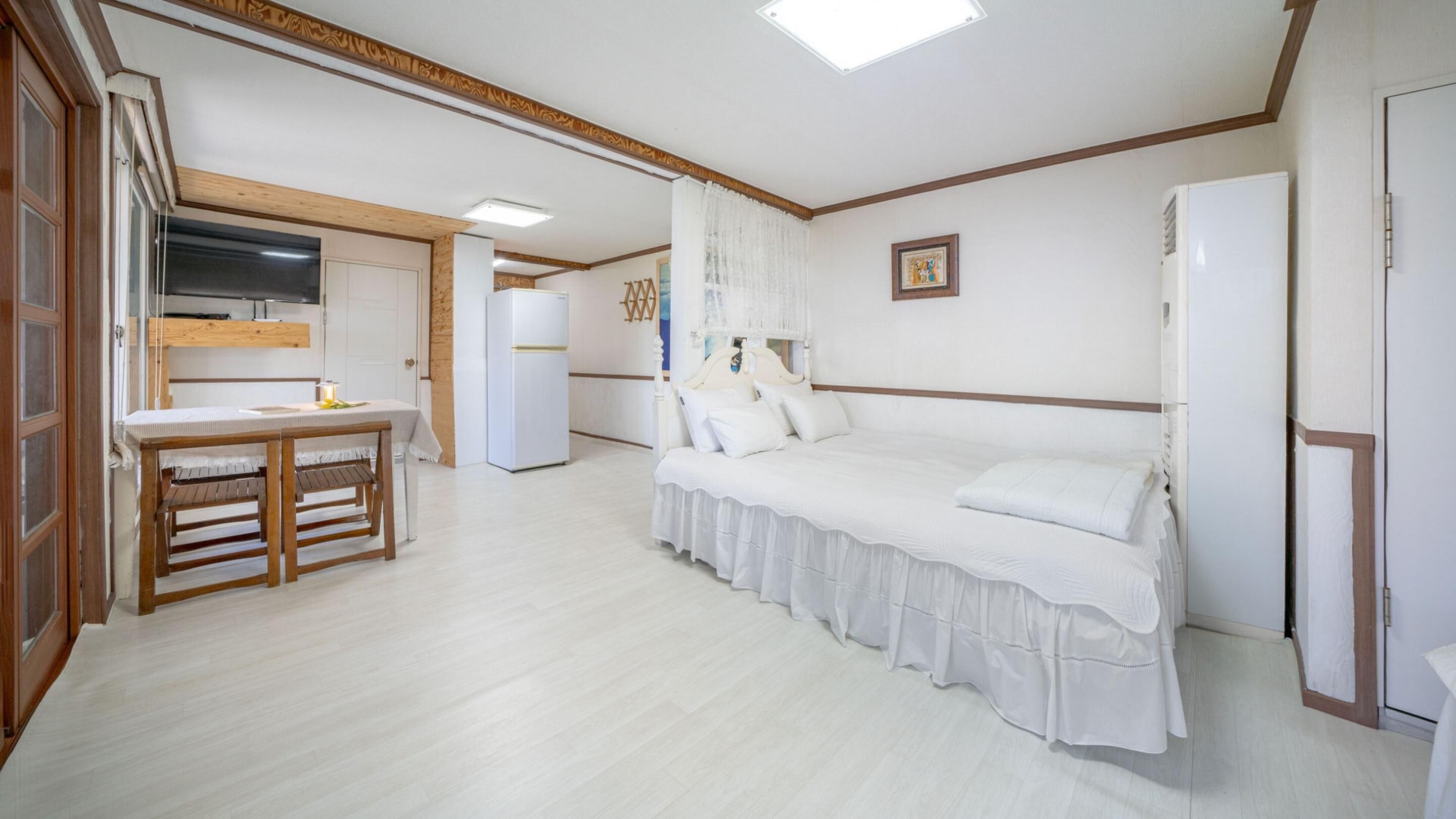 Un dormitorio con cama, mesita de noche, silla, armario y una zona de cocina con refrigerador y lavabo.
