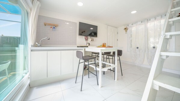 Una cocina moderna con armarios blancos, una mesa de comedor con cuatro sillas, un horno empotrado y un ventanal con vistas a un balcón.