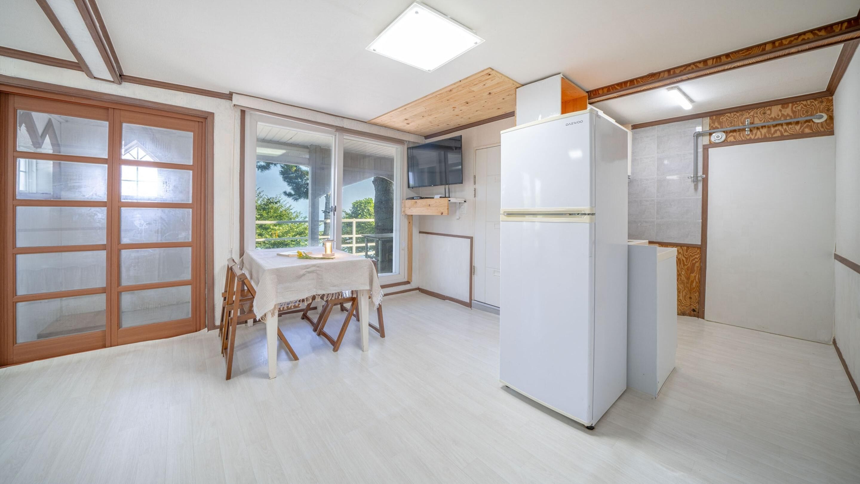 A kitchen with a dining table, a refrigerator, and a window with a view of greenery.