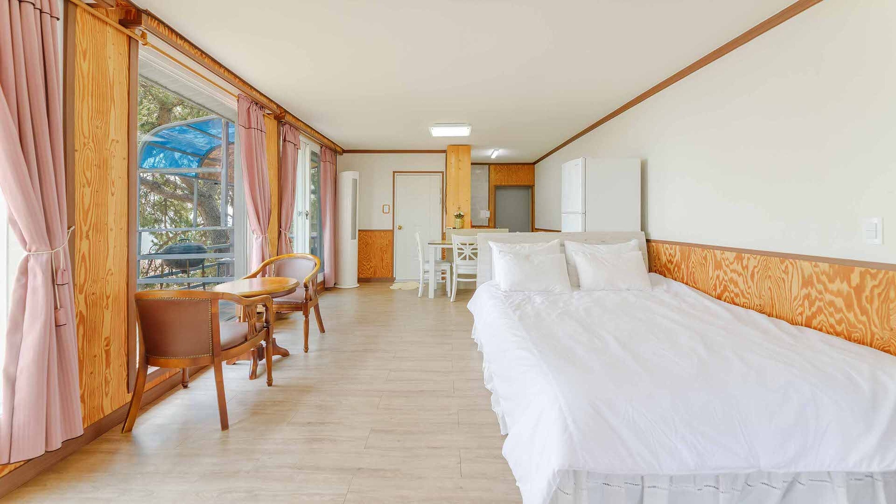 Une chambre d’hôtel avec un grand lit, un bureau en bois, une chaise et une vue dégagée sur l’extérieur grâce à une grande fenêtre.