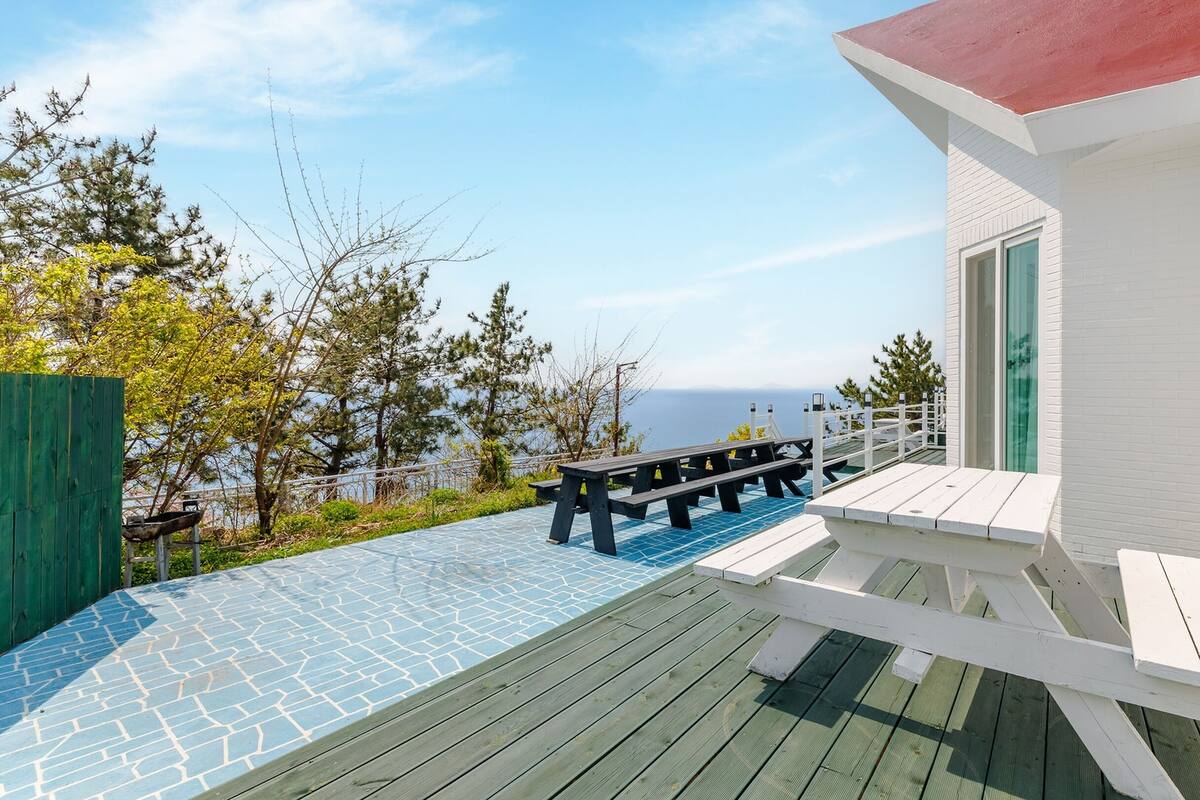A wooden deck with a blue-tiled patio area, white walls, and a red roof.