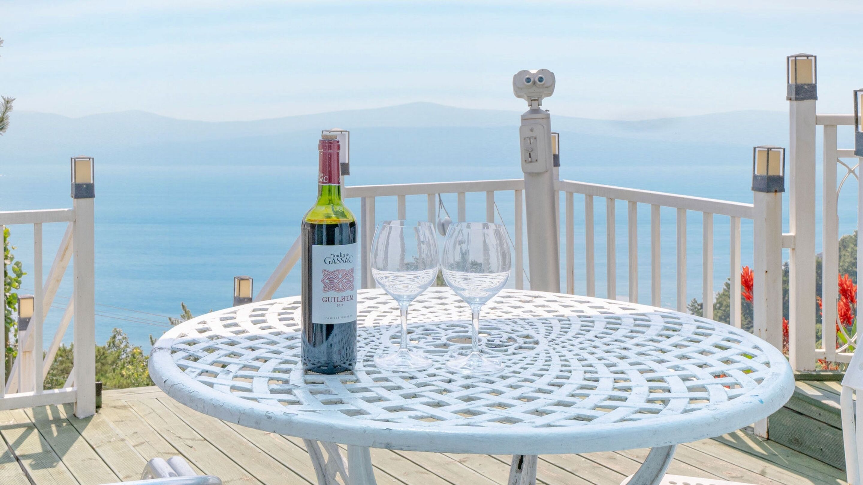 Une table avec une bouteille de vin et deux verres, placée sur une terrasse offrant une vue sur la mer.