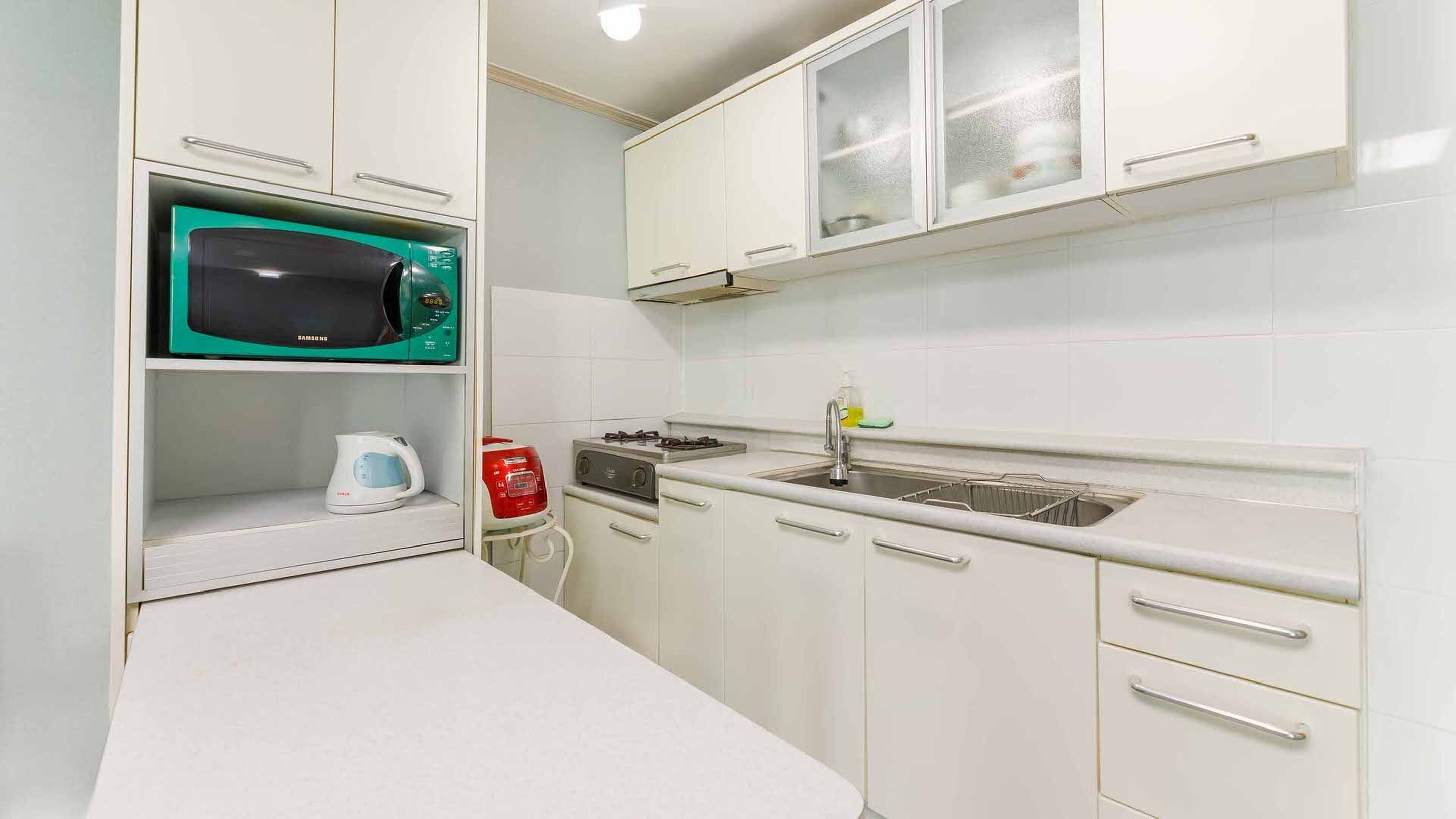 A compact kitchen with white cabinets, a microwave, a kettle, and a gas stove.