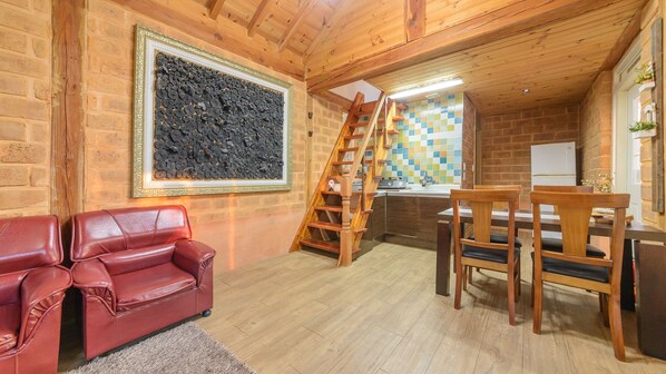 A cozy log cabin interior with a red leather sofa, a wooden dining table with chairs, a staircase, and a large decorative wall piece. - Gapyeong Ebenzer Pension (Gapyeong)