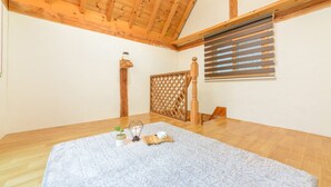 A room with wooden flooring, a white wall, a wooden ceiling, a window with blinds, a small table with a cup and a plant, and a white rug. - Gapyeong Ebenzer Pension (Gapyeong)