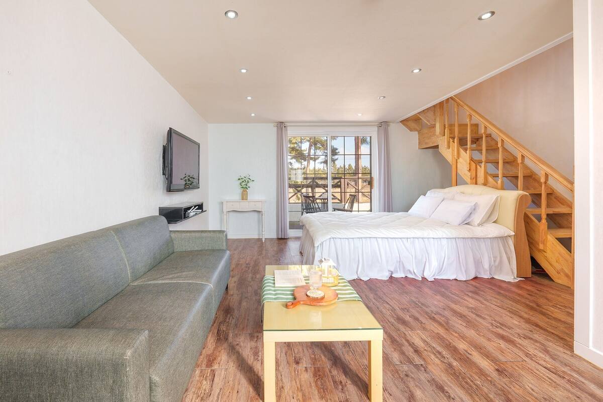 A modern bedroom with a wooden staircase, a sofa, a bed, and a small table with a tray.