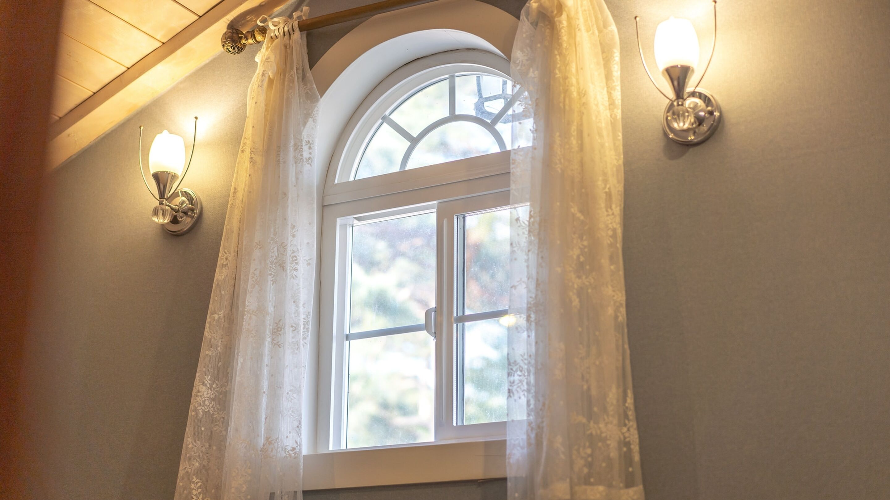 A bathroom with a window, two wall-mounted lights, and a wooden ceiling.