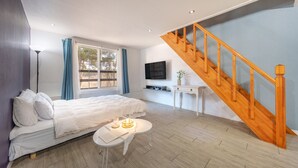 A bedroom with a bed, a bedside table, a lamp, a TV mounted on the wall, and a wooden staircase. - The Gangneung Foret Pension (Gangneung)
