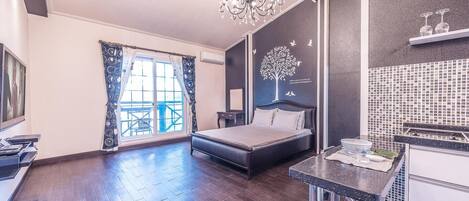 A modern bedroom with a large bed, a chandelier, a view of the outdoors, and a kitchen area with a sink and countertop.