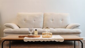 A wooden table with a lace tablecloth, a glass, a bottle, and a wooden lantern on a wooden floor with a beige sofa in the background. - The Gangneung Foret Pension (Gangneung)