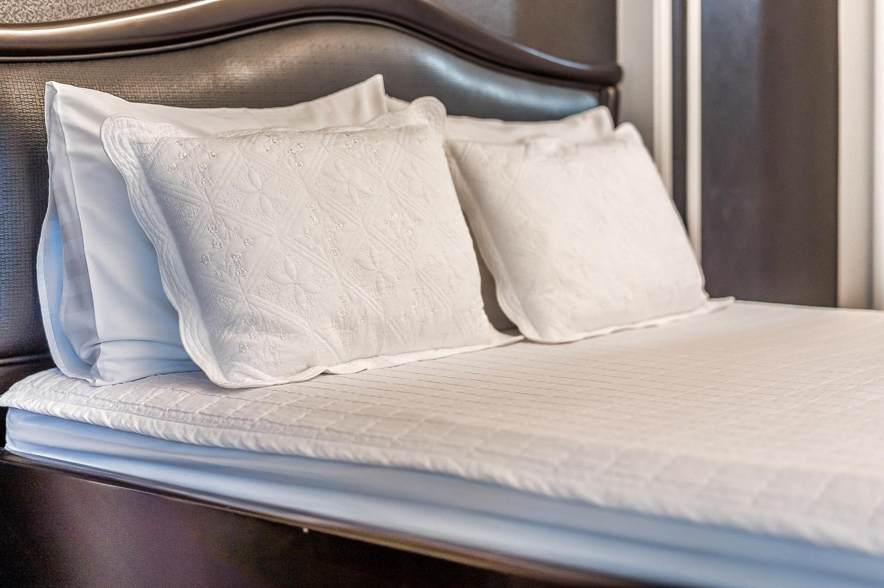 A neatly made bed with white linens and pillows, a dark headboard, and a wooden nightstand.