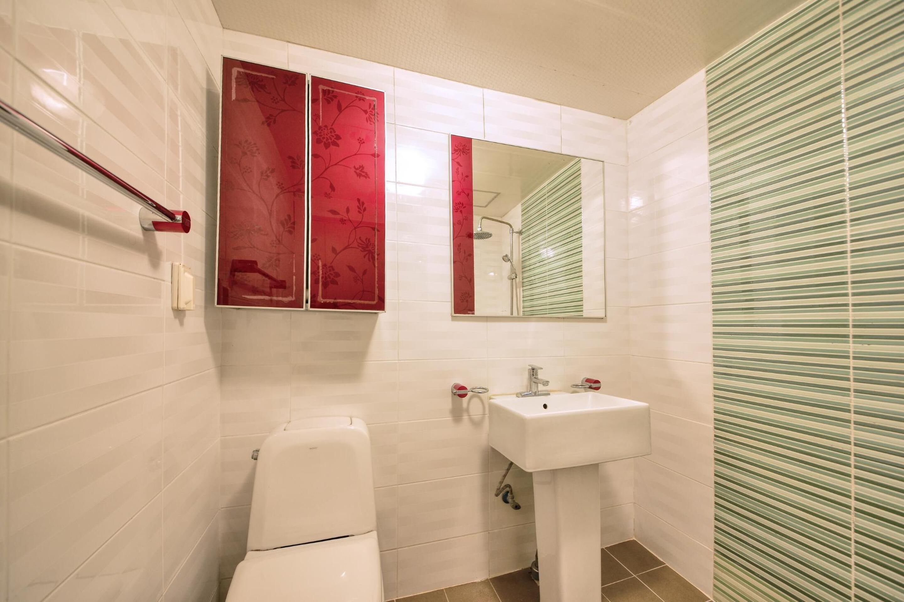 A bathroom with white tiled walls, a white toilet, a sink, and a shower.