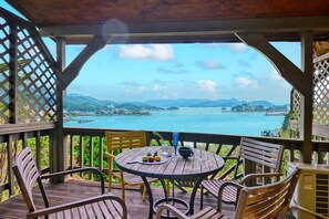 Une terrasse en bois avec une table ronde et des chaises, d’où l’on peut admirer un plan d’eau et un paysage lointain.