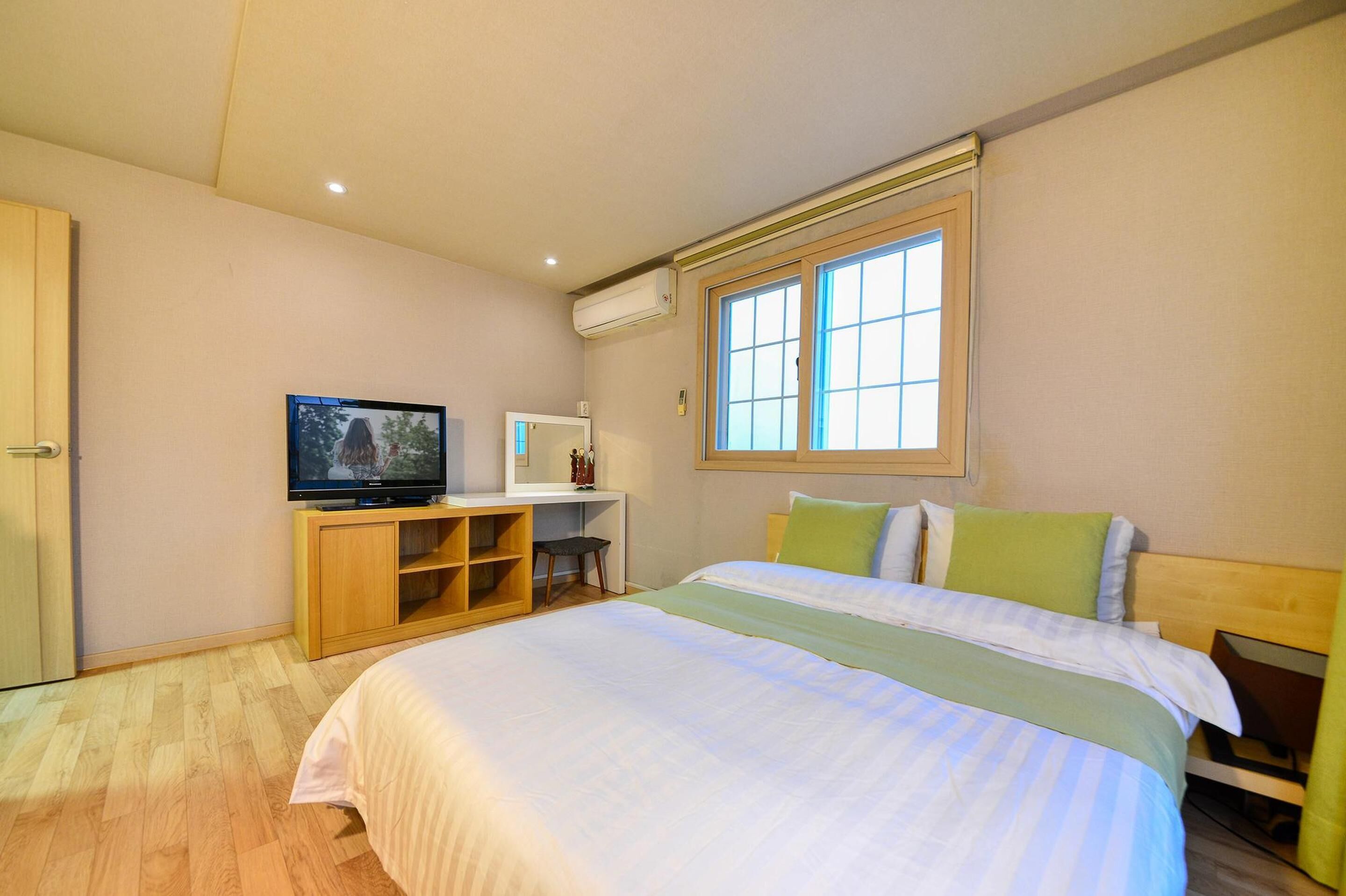 Un dormitorio con cama, televisión, escritorio y ventana.