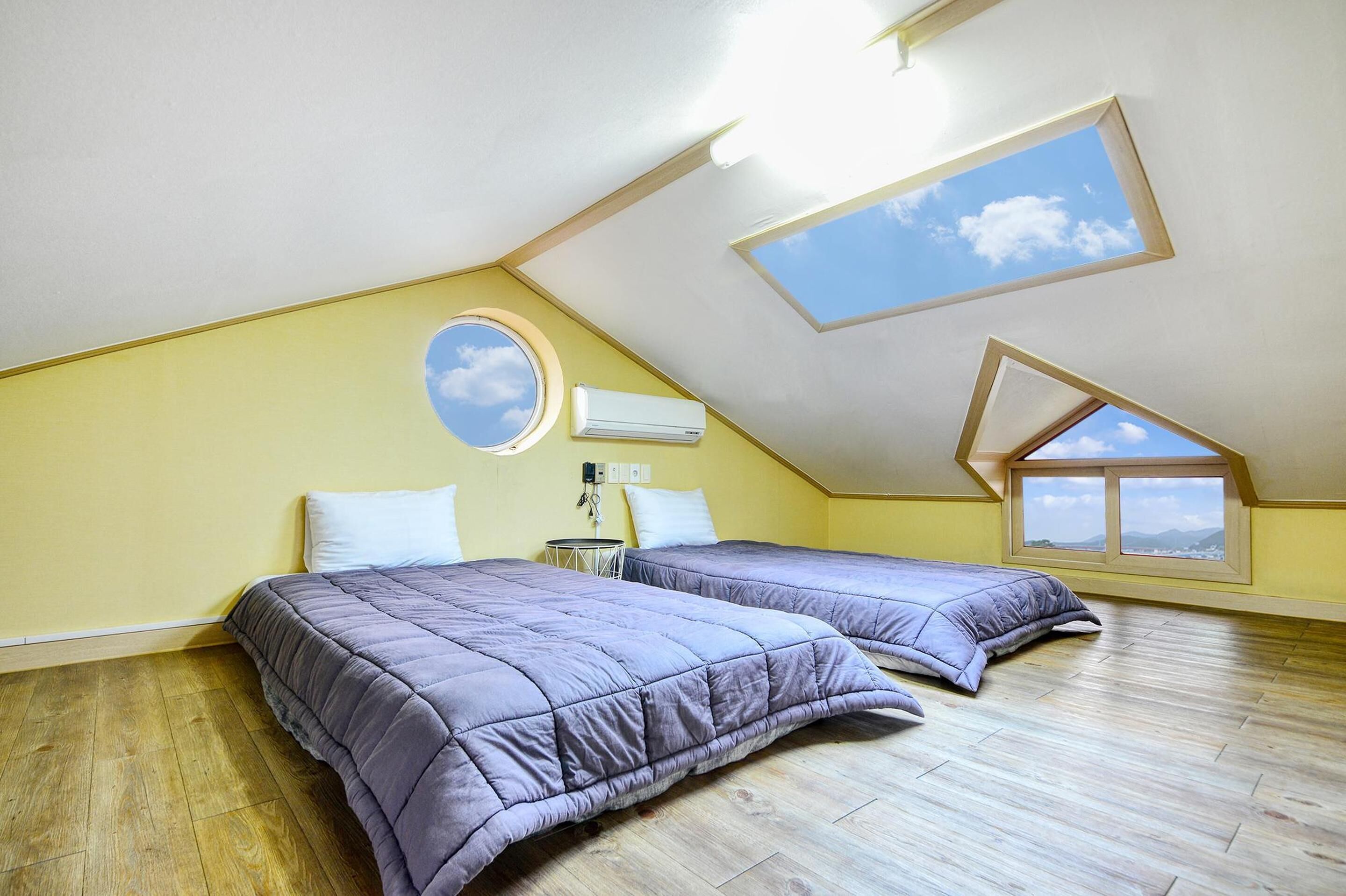 Une chambre avec deux lits, une lucarne et une vue sur le ciel.