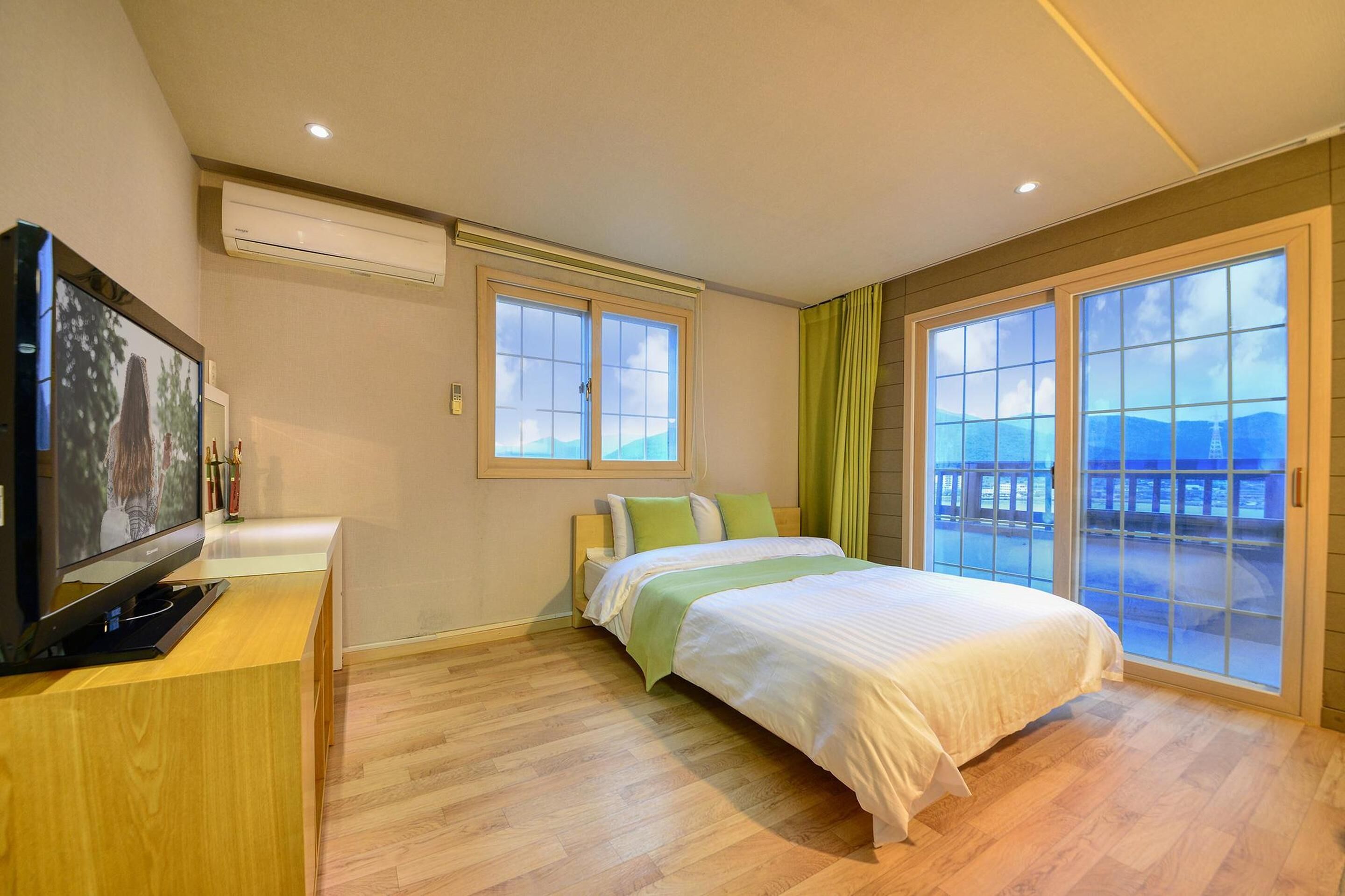 A hotel room with a bed, a TV, and a view of the outdoors.